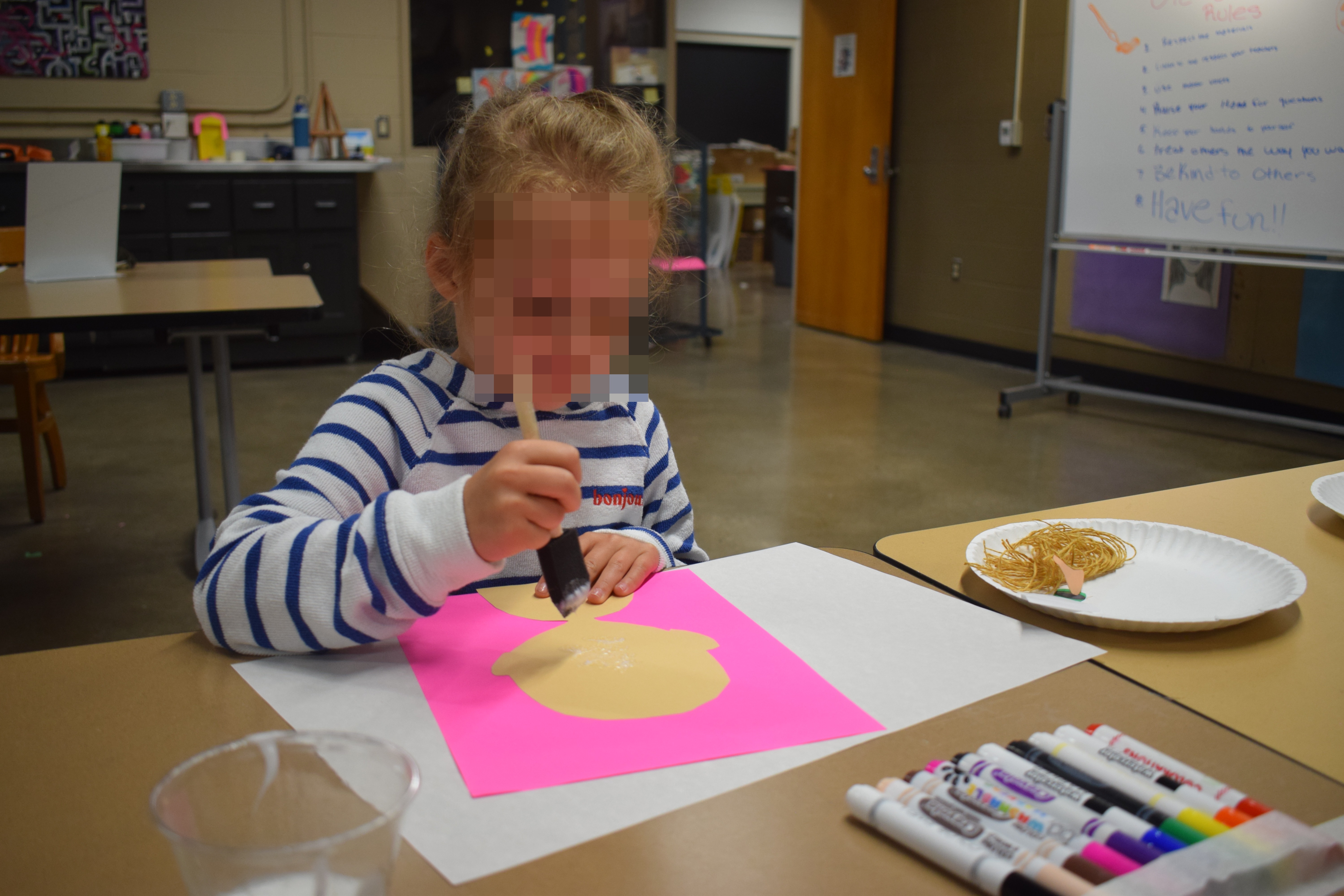 Young student using glue and a stencil to create the `Surface` layer of her identity portrait on pink paper.